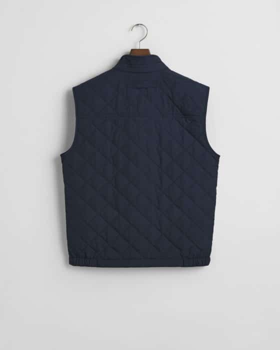 Navy blue quilted vest with a high collar, sleeveless design, and a diamond pattern, displayed on a wooden hanger against a white background, shown from the back.