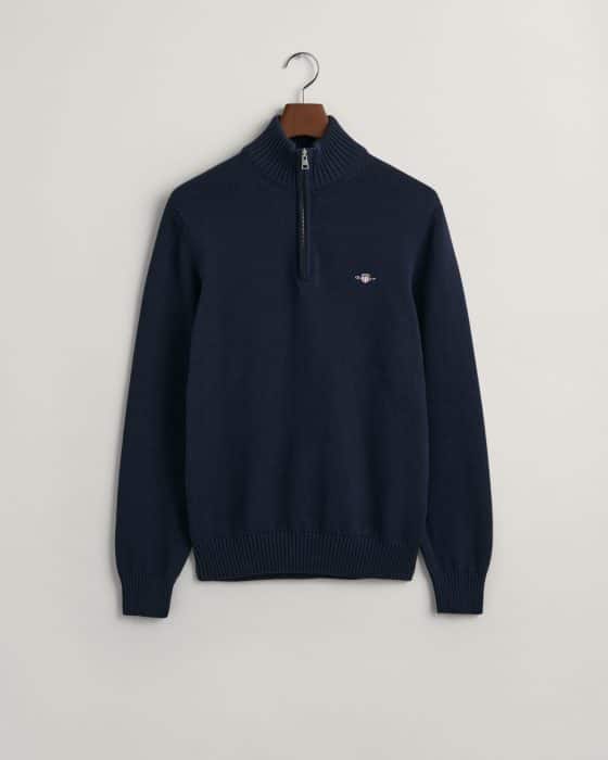 A navy blue quarter-zip sweater with a ribbed collar, cuffs, and hem, hanging on a wooden hanger against a plain light background. There is a small embroidered logo on the left chest.