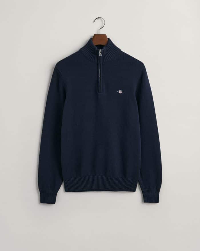 A navy blue quarter-zip sweater with a ribbed collar, cuffs, and hem, hanging on a wooden hanger against a plain light background. There is a small embroidered logo on the left chest.