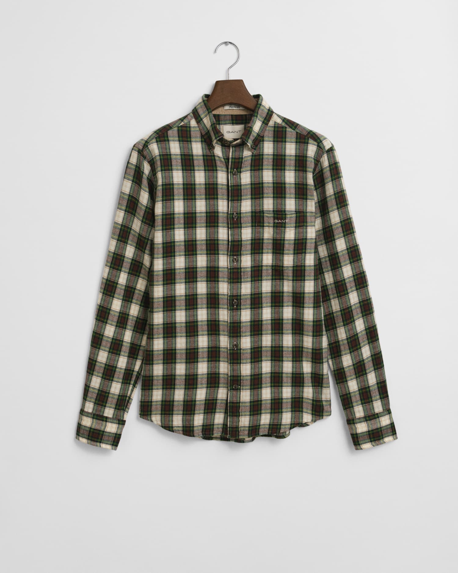 A long-sleeved, button-up flannel shirt with a green, black, and white plaid pattern hangs on a wooden hanger against a plain white background.