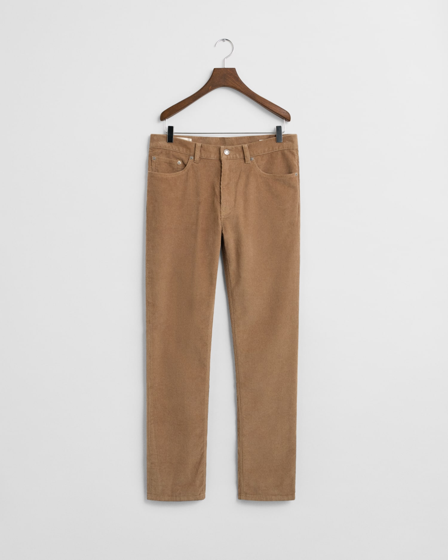 A pair of tan corduroy pants with front and back pockets hangs on a wooden hanger against a plain white background.
