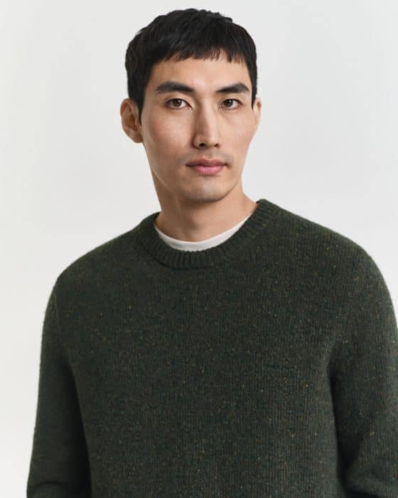 A man with short black hair and wearing a dark green sweater stands against a plain white background, looking calmly at the camera.