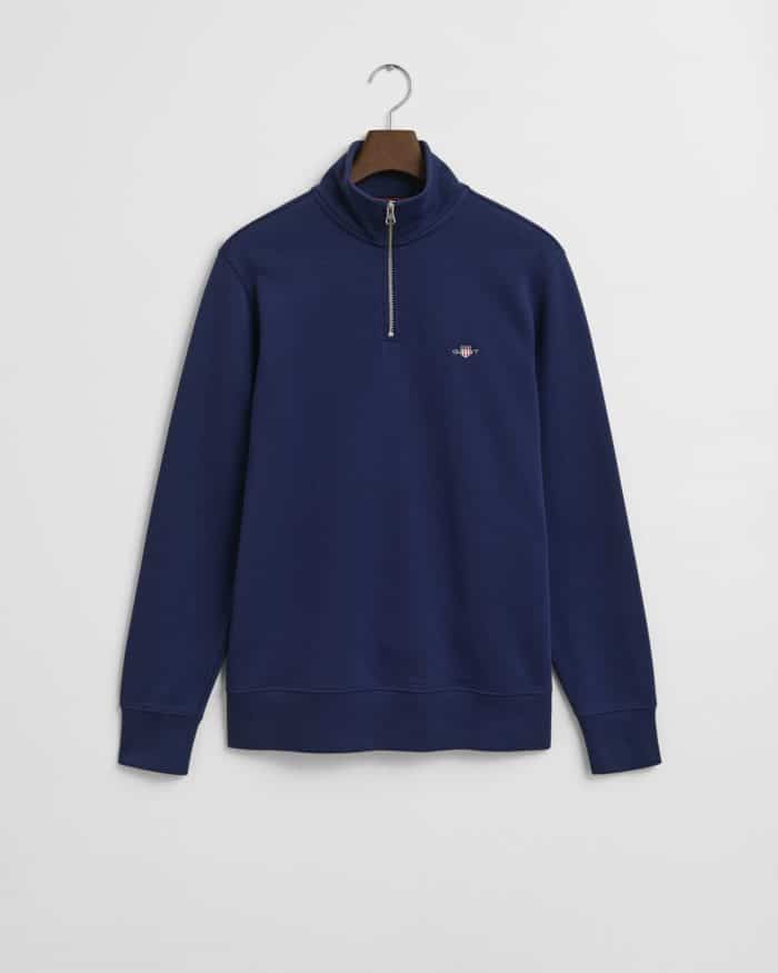 A navy blue quarter-zip pullover sweatshirt with a small embroidered logo on the left chest, hanging on a wooden hanger against a white background.