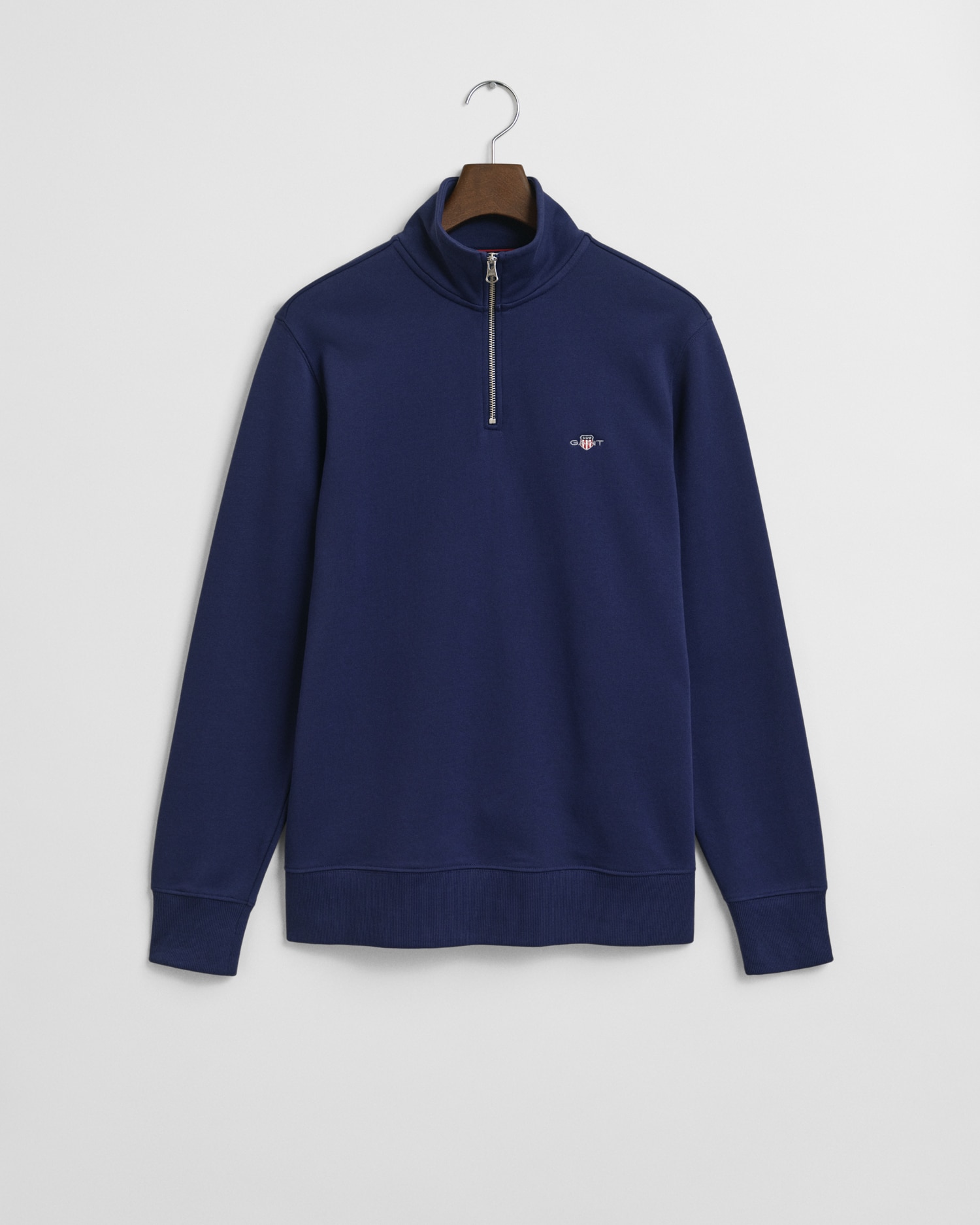 A navy blue quarter-zip pullover sweatshirt with a small embroidered logo on the left chest, hanging on a wooden hanger against a white background.