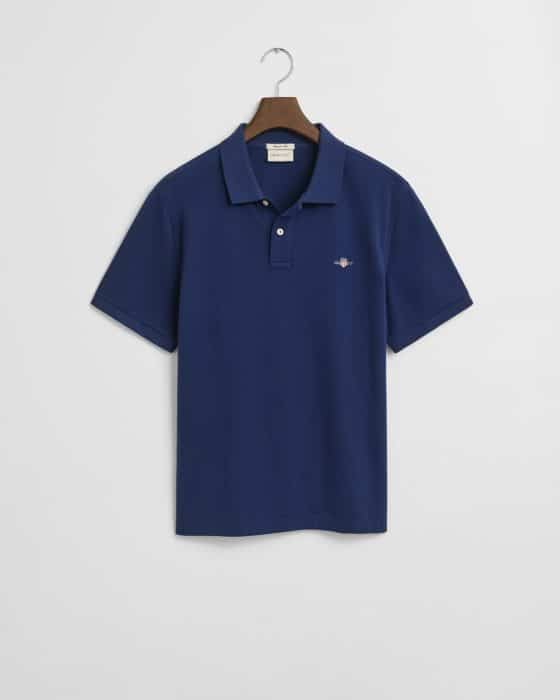 A navy blue short-sleeve polo shirt hangs on a wooden hanger against a white background. The shirt features a small embroidered logo on the left chest and a classic collar with a button placket.