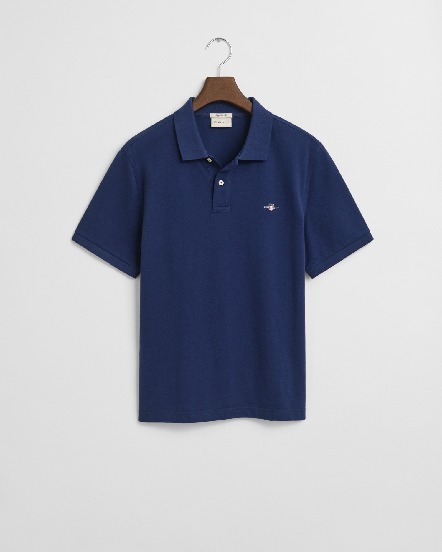 A navy blue short-sleeve polo shirt hangs on a wooden hanger against a white background. The shirt features a small embroidered logo on the left chest and a classic collar with a button placket.