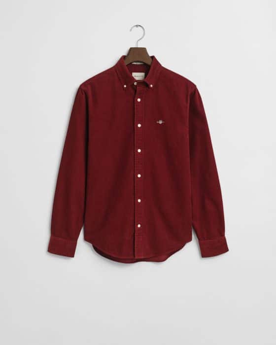 A long-sleeved, button-down corduroy shirt in deep red, displayed on a hanger against a plain white background. The shirt features a small embroidered logo on the left chest.