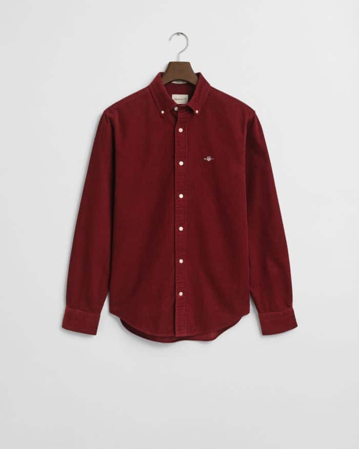 A long-sleeved, button-down corduroy shirt in deep red, displayed on a hanger against a plain white background. The shirt features a small embroidered logo on the left chest.