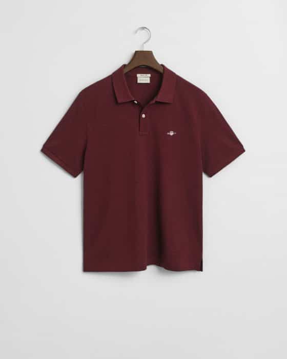 A maroon short-sleeve polo shirt with a collar, two buttons, and a small embroidered logo on the left chest, hanging on a hanger against a white background.
