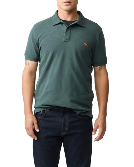 A person wearing a forest green short-sleeve polo shirt with a small orange animal logo on the chest and dark blue jeans, standing against a white background.
