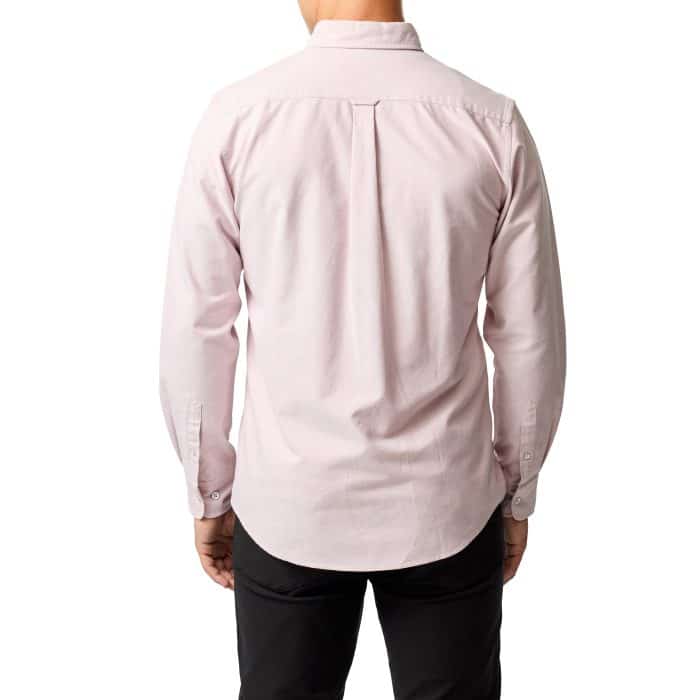 A person stands facing away, wearing a light pink long-sleeve button-up shirt and black pants against a white background.