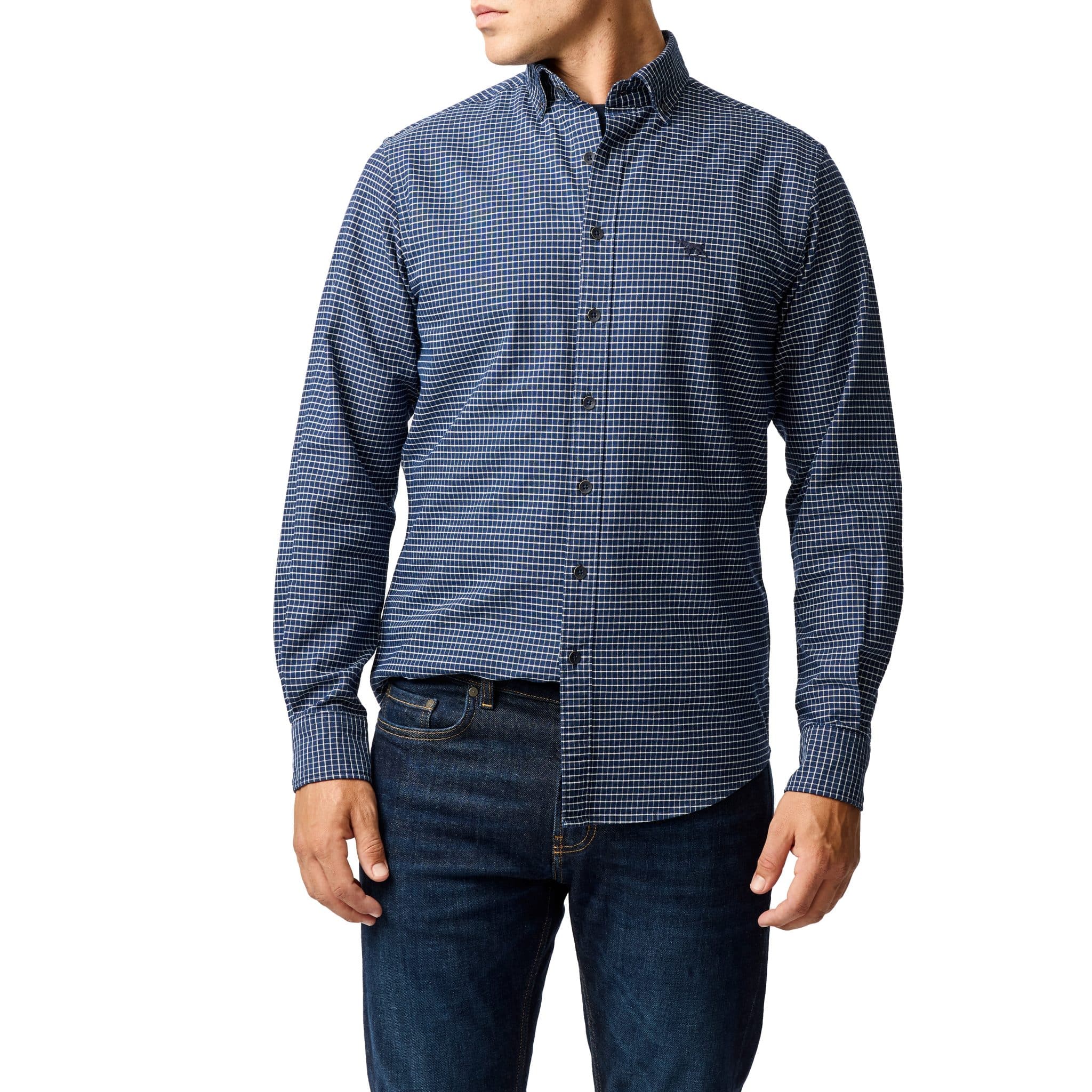 A person wearing a blue and black checkered long-sleeve button-down shirt and dark blue jeans, standing against a white background. The persons head is turned slightly to the side.