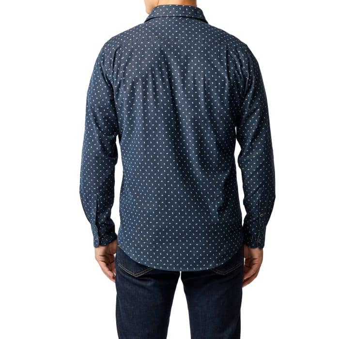A man is standing with his back to the camera, wearing a navy blue long-sleeve shirt with a small white polka dot pattern and dark blue jeans.