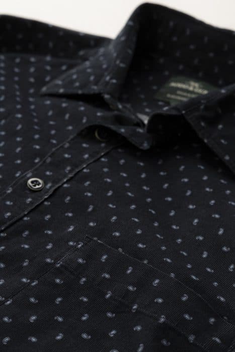 Close-up of a dark-colored button-up shirt with a subtle light dot pattern and a front pocket, lying flat on a surface.