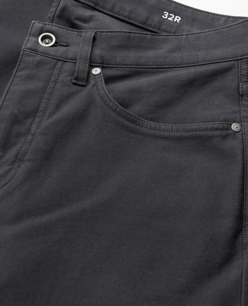 Close-up of the front pocket area of a pair of black jeans with visible stitching, metal rivets, a belt loop, and a button. The waistband is marked with the size 32R in white text.