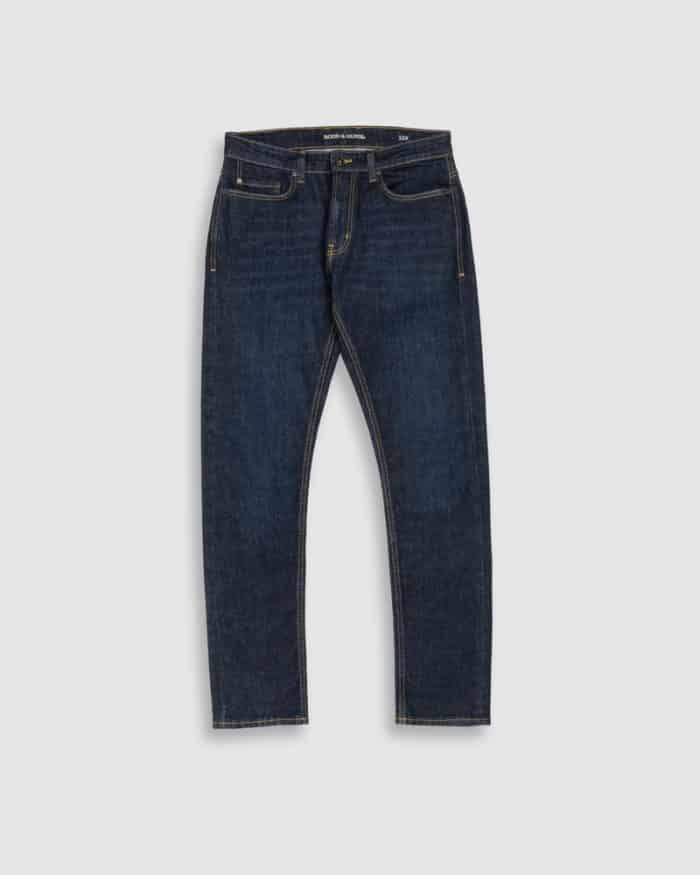 A pair of dark blue denim jeans with a slim fit, classic five-pocket design, and visible tan stitching, displayed against a light gray background.
