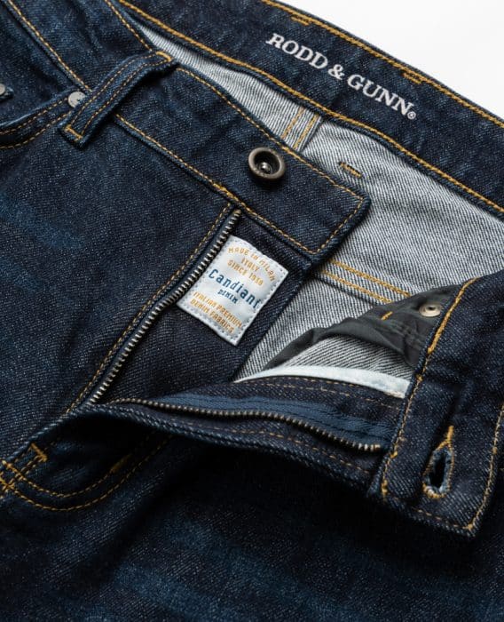 Close-up of dark blue Rodd & Gunn jeans with copper stitching, unzipped to show a label reading Made in Turkey exclusively for Rodd & Gunn by Candiani, premium Italian denim.