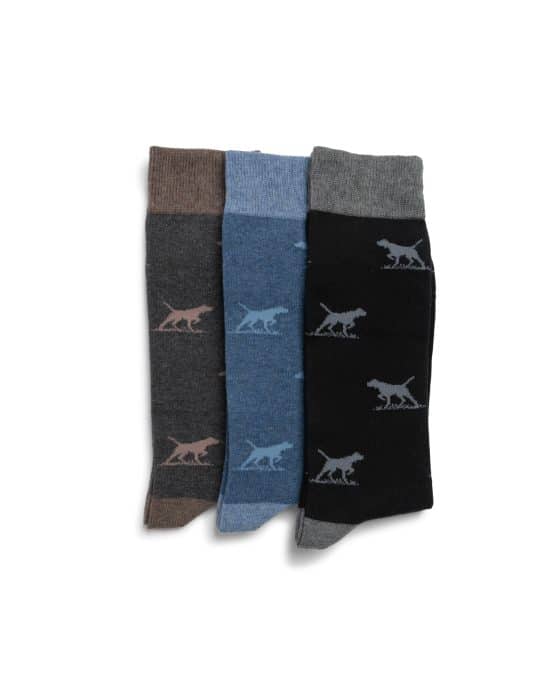 Three pairs of socks in dark grey, blue, and black, each with a contrasting dinosaur pattern, are laid side by side on a white background.