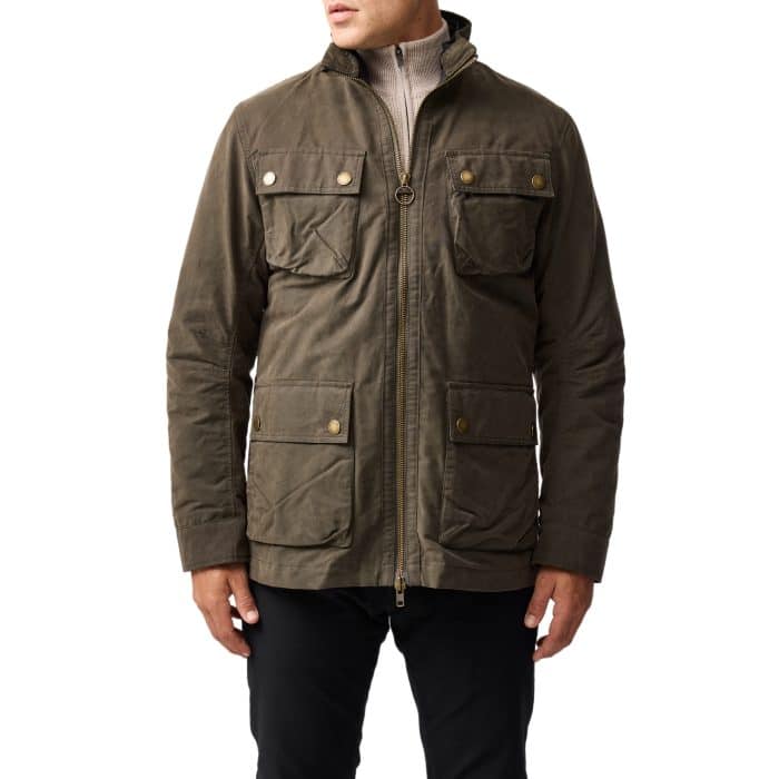 A person wearing a khaki green field jacket with a stand collar, zip and snap closures, and four front flap pockets, paired with black pants. The persons head is not visible.
