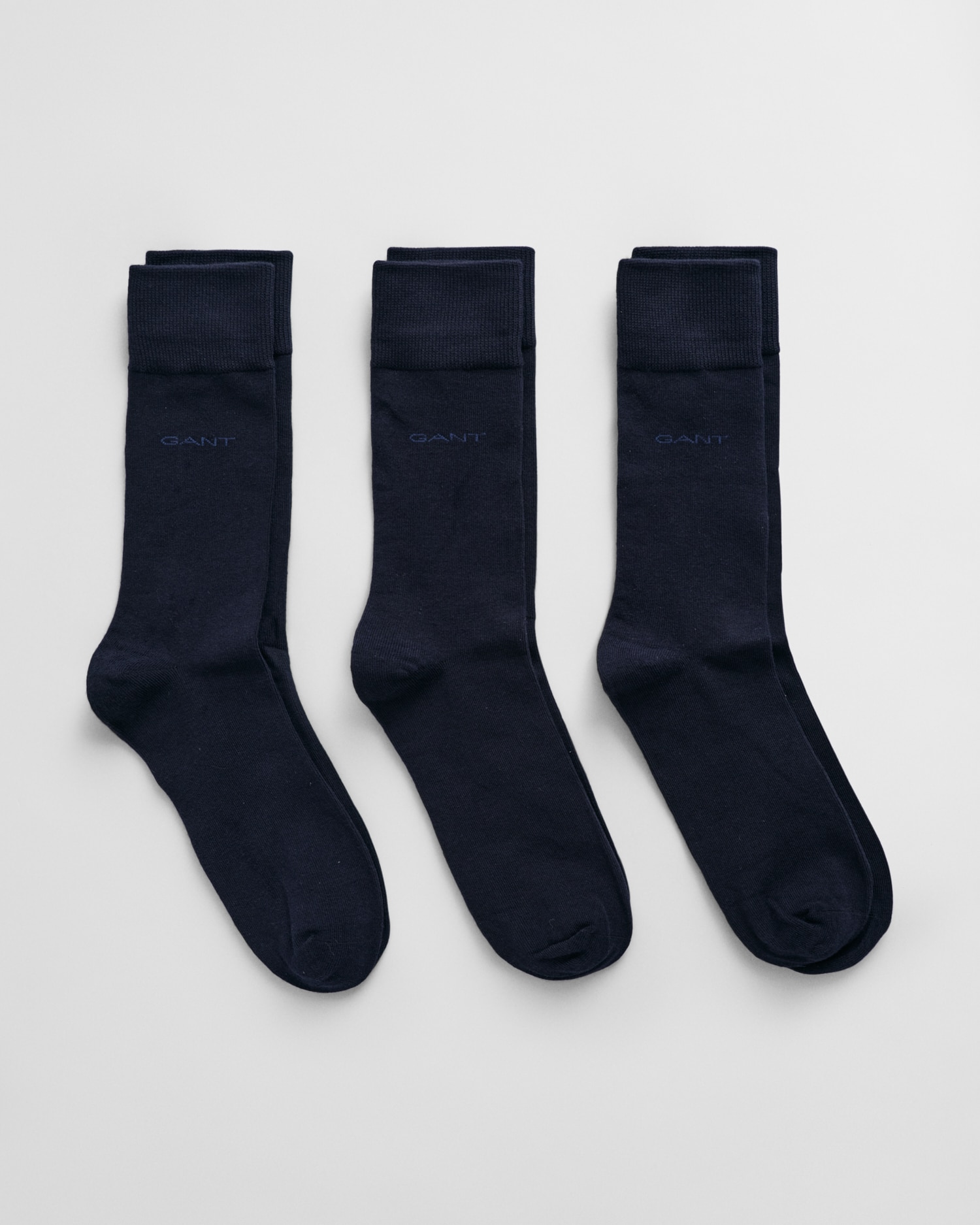 Three pairs of neatly folded dark navy socks are laid side by side on a light gray background. Each sock has a subtle GANT logo near the top.