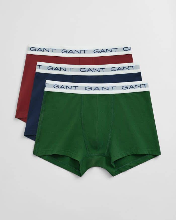 Three pairs of mens boxer briefs in green, navy blue, and maroon, each with a white waistband featuring the word GANT in blue lettering, laid out overlapping on a white background.
