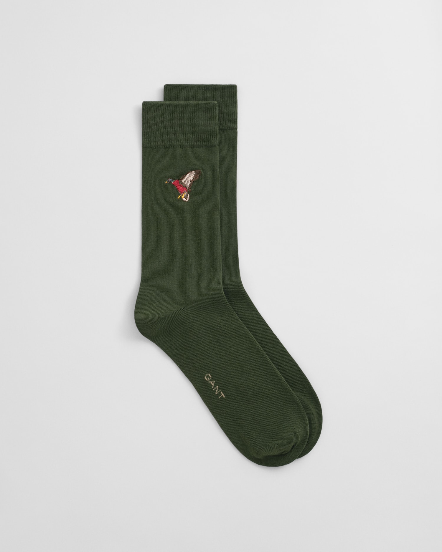 A pair of dark green socks with a small embroidered mushroom design near the top and the word GANT printed near the toe on a plain white background.