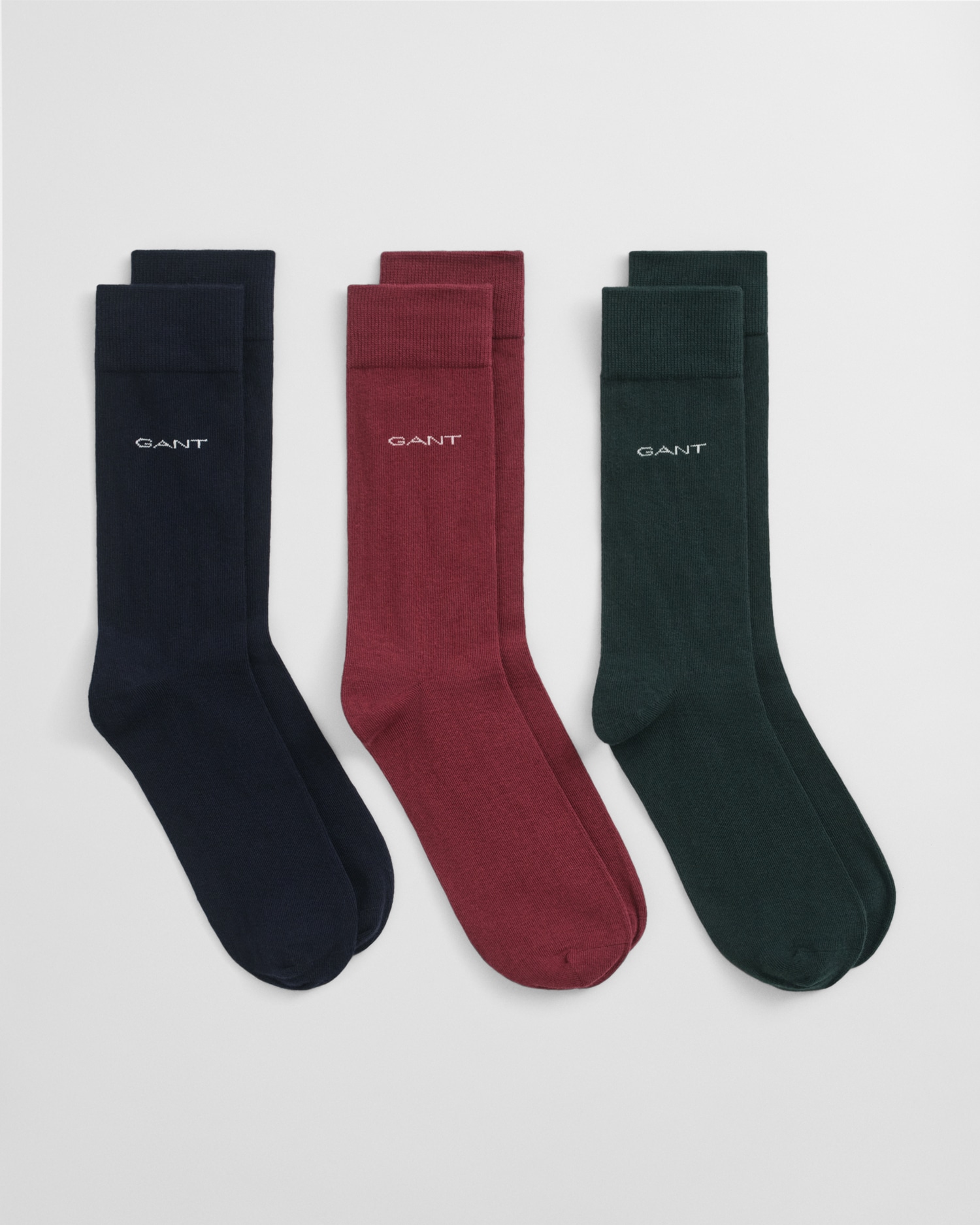 Three pairs of GANT socks in navy blue, burgundy, and dark green, each with the brand name embroidered near the top, displayed side by side on a white background.