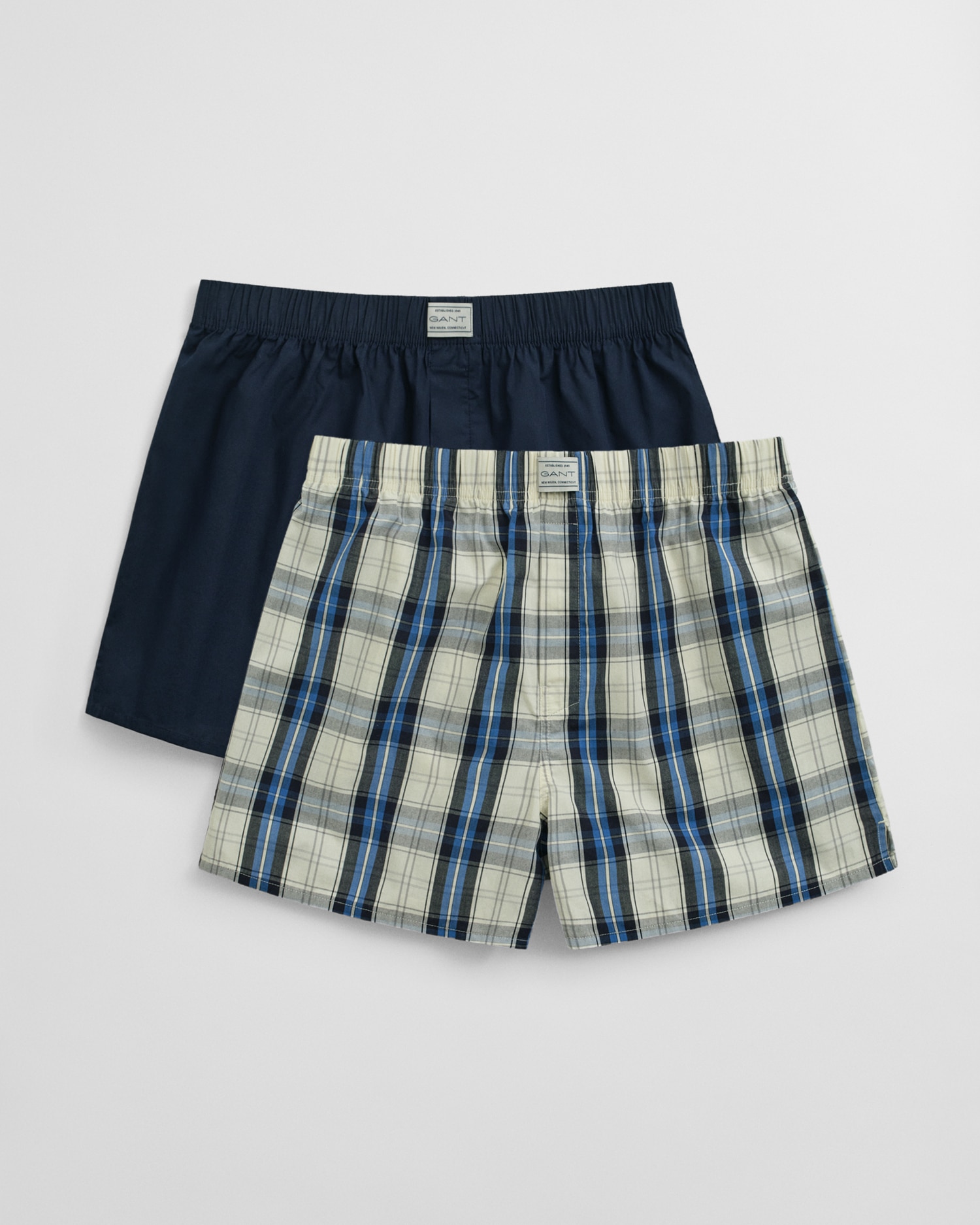 Two pairs of mens boxers: one solid navy blue, and one with a blue, black, and white plaid pattern, both with elastic waistbands and displayed on a plain white background.