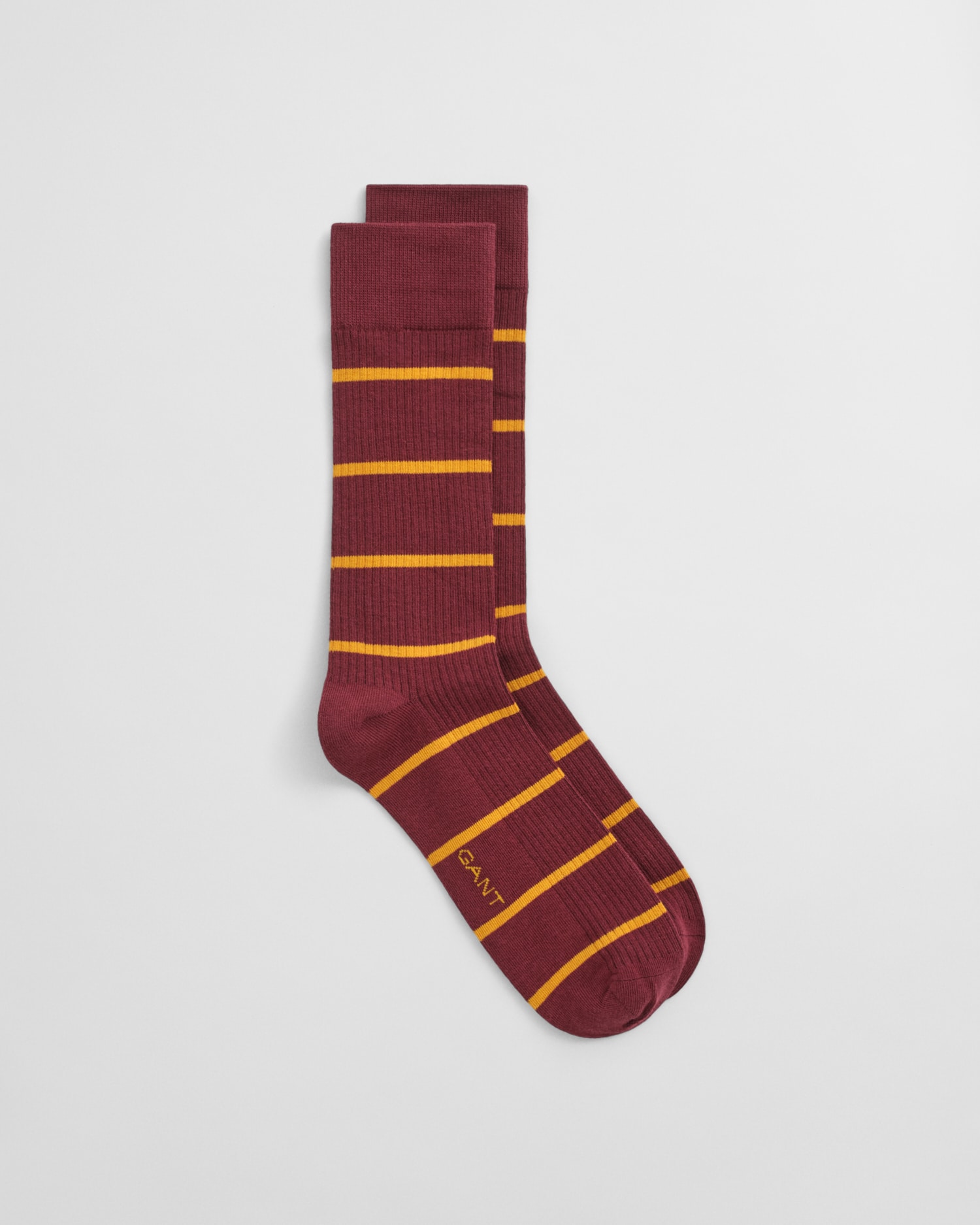 A pair of maroon socks with horizontal yellow stripes and the word GANT written near the toe, displayed on a plain white background.
