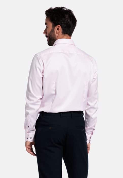 A man with dark hair is shown from the back, wearing a light pink dress shirt and dark trousers against a plain white background.