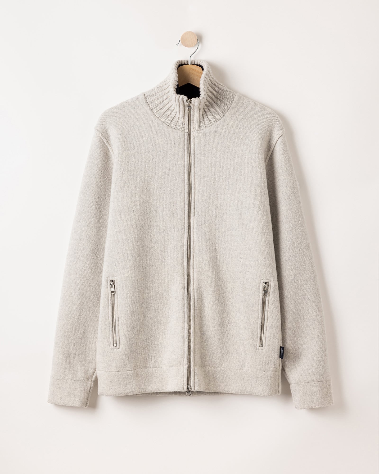 A light gray zip-up sweater with a ribbed high collar and two front zippered pockets, hanging on a wooden hanger against a plain white background.