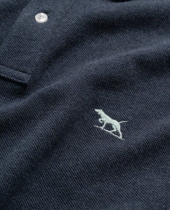 Close-up of a dark textured polo shirt with a white button and an embroidered light-colored dog logo on the fabric.