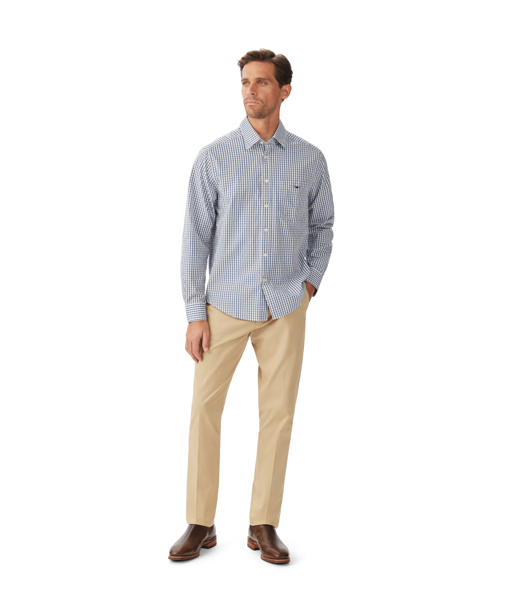 A man stands against a white background wearing a blue and white checkered button-down shirt, beige pants, and brown dress shoes. He has short hair and is looking slightly to his right.