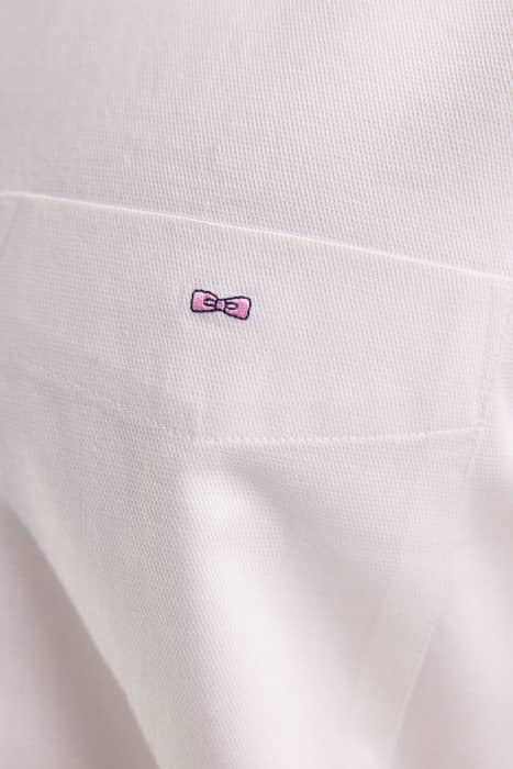 Close-up of a white fabric with a textured pattern, featuring a small embroidered pink bow with black outline and detail near the top center.