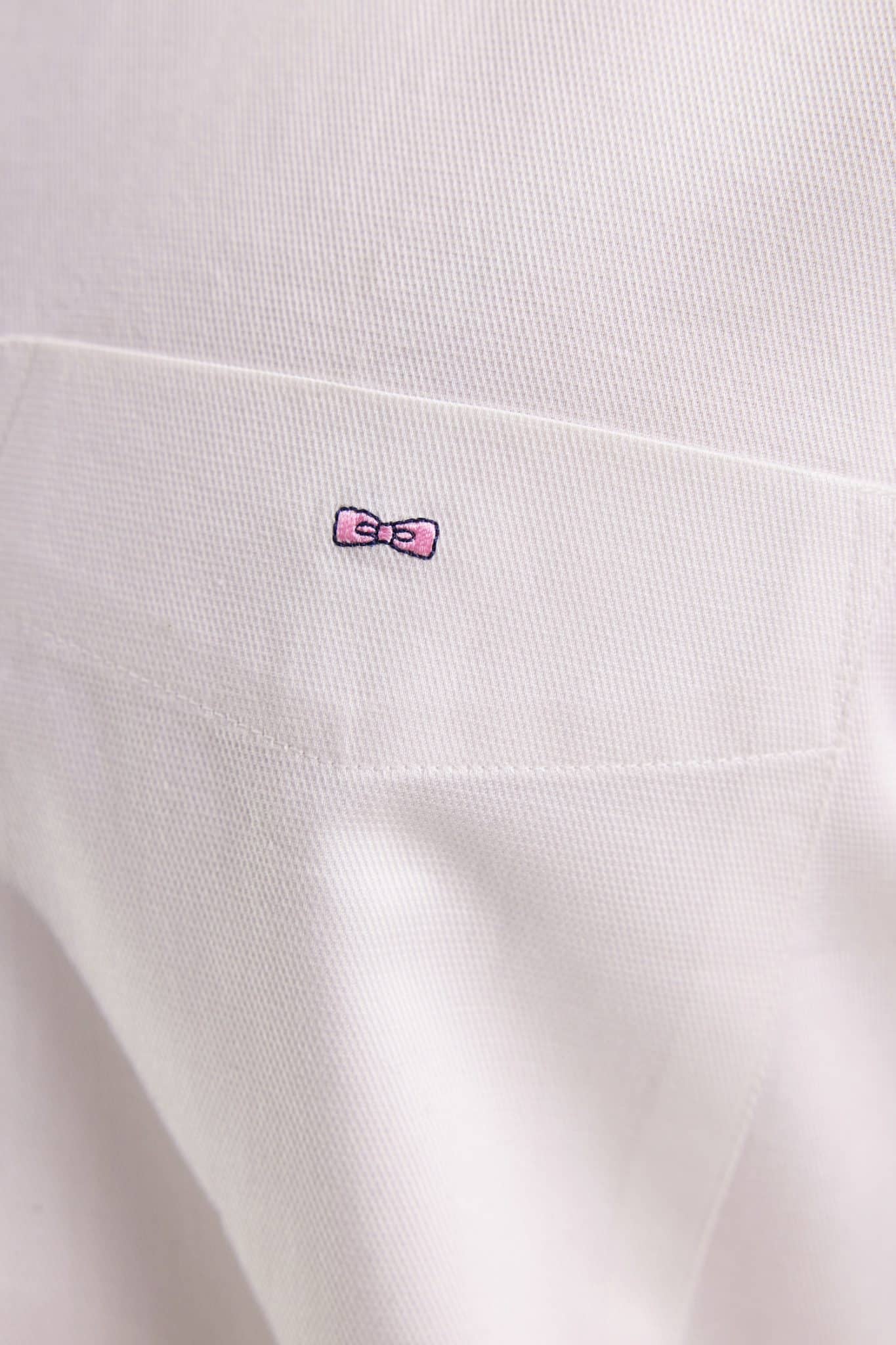 Close-up of a white fabric with a textured pattern, featuring a small embroidered pink bow with black outline and detail near the top center.
