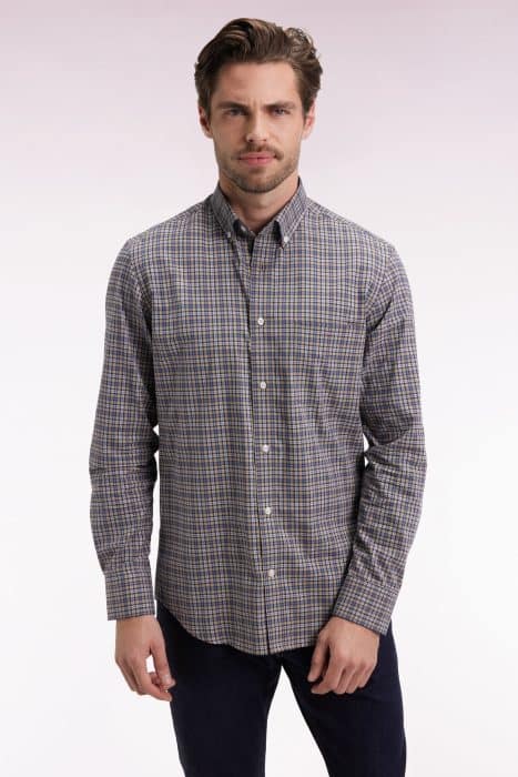 A man with light brown hair and a short beard is wearing a long-sleeve, button-up plaid shirt in shades of blue, brown, and white, standing against a light, gradient background.