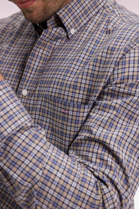 A close-up of a person wearing a blue and beige plaid button-up shirt with a front pocket and a visible collar. The persons face is partially out of the frame.