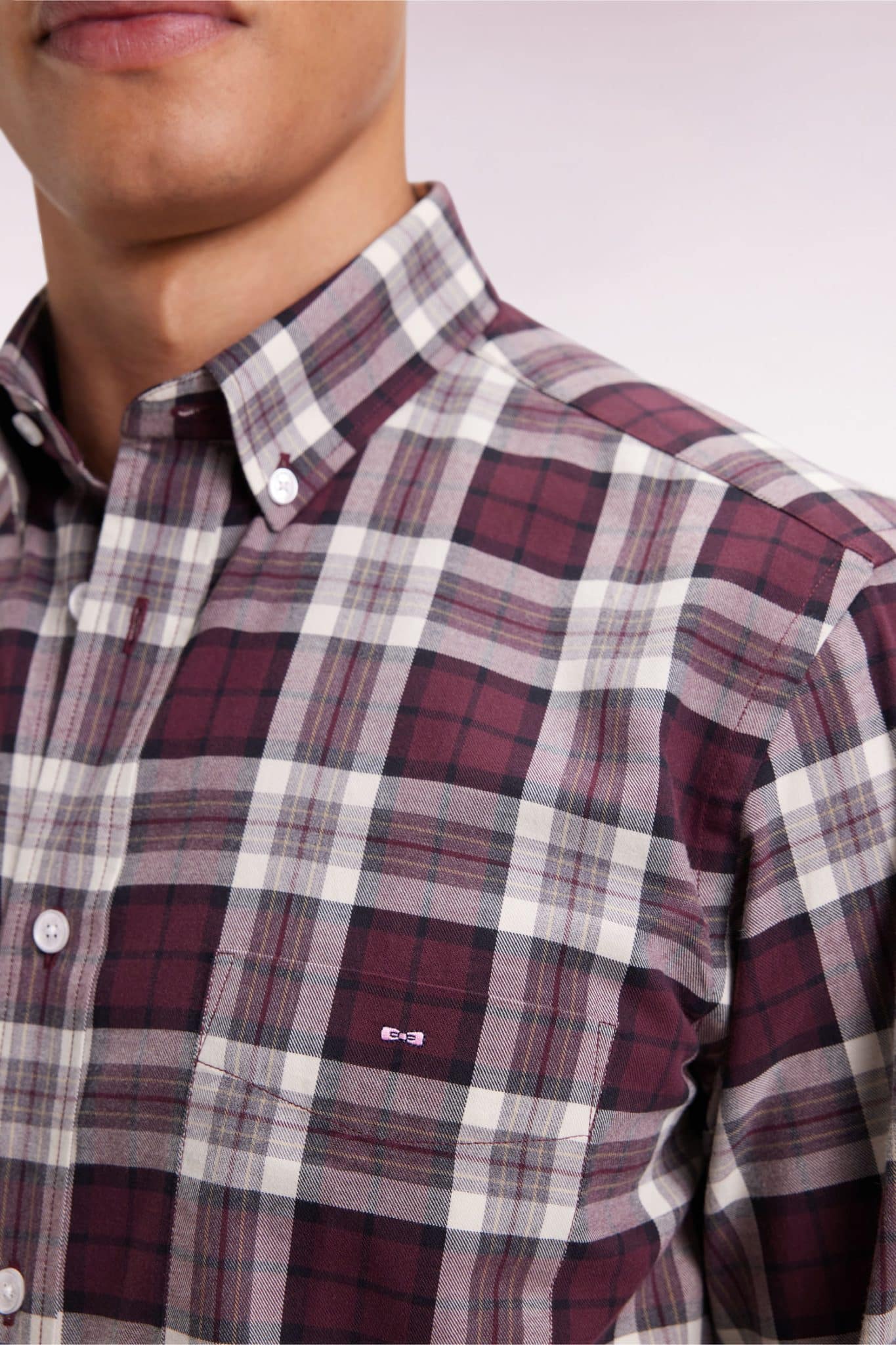 A person wearing a button-up shirt with a burgundy, white, and gray plaid pattern. The image is cropped at the chest, showing the shirts pocket and collar.