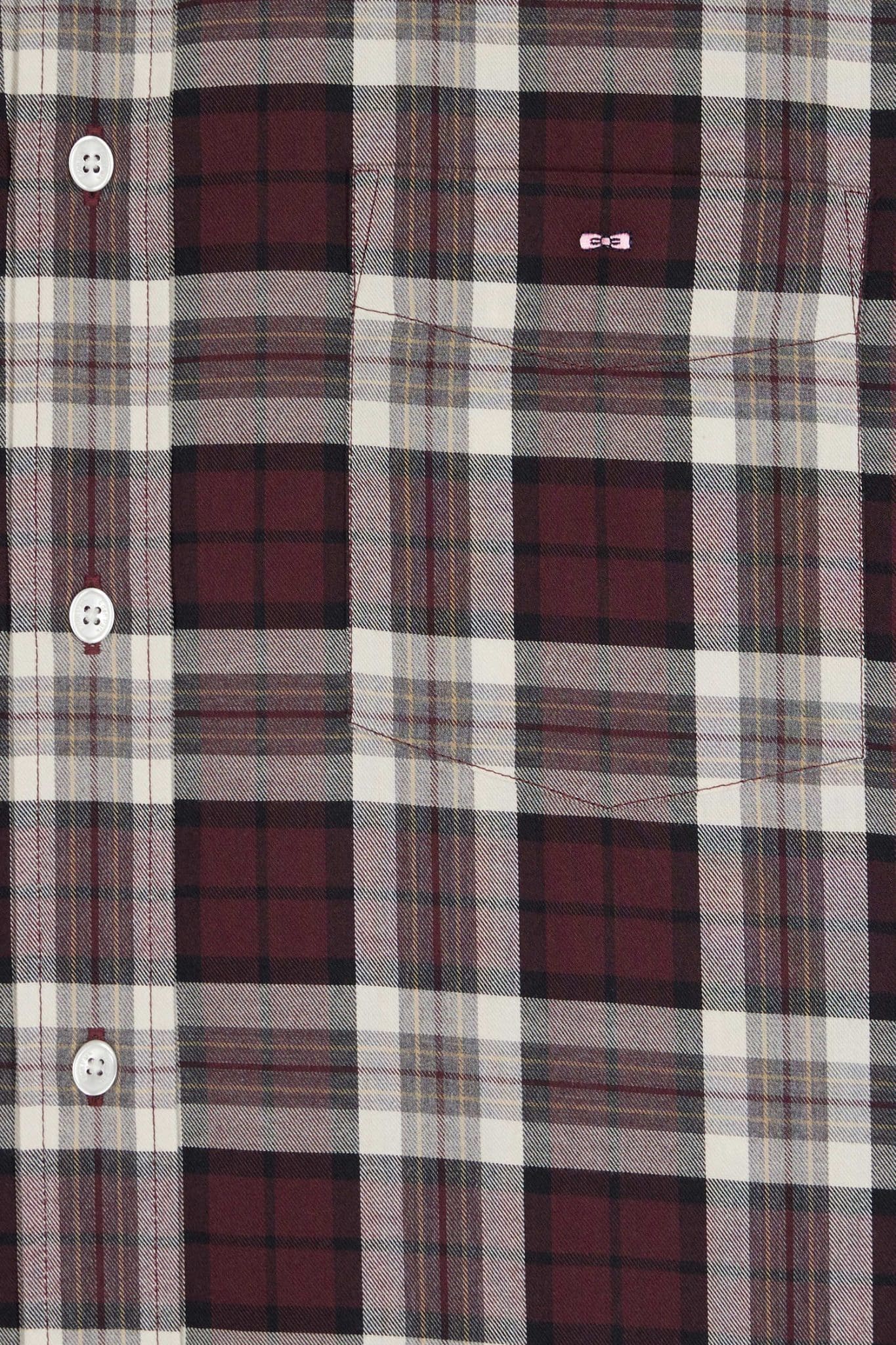 Close-up of a maroon, black, white, and gray plaid shirt with white buttons and a front pocket. The fabric features a checkered pattern and a small stitched detail above the pocket.