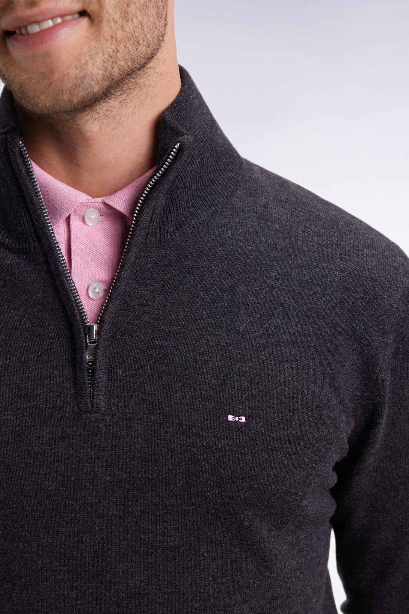 A man wearing a dark gray quarter-zip sweater over a light pink collared shirt. Only the lower half of his face and upper torso are visible. The sweater has a small embroidered logo on the chest.