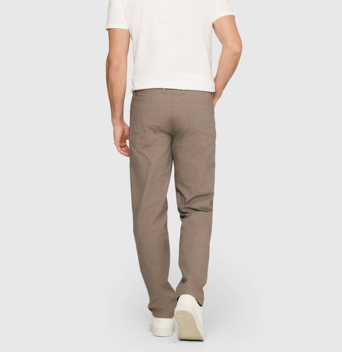 A man wearing a white short-sleeve shirt, light brown trousers, and white shoes is standing with his back to the camera against a plain light grey background.