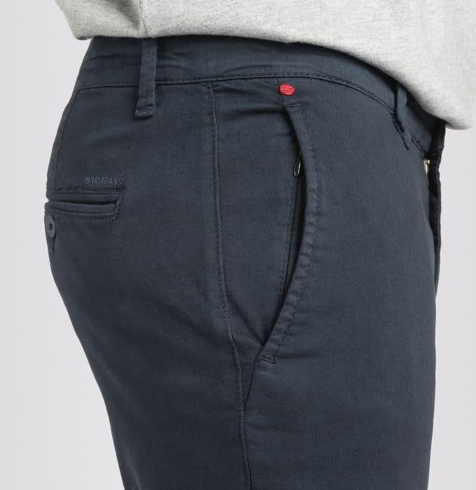 Close-up of a person wearing dark navy trousers with a side pocket, visible stitching, and a small red button detail near the waistband; part of a light grey shirt is also visible.