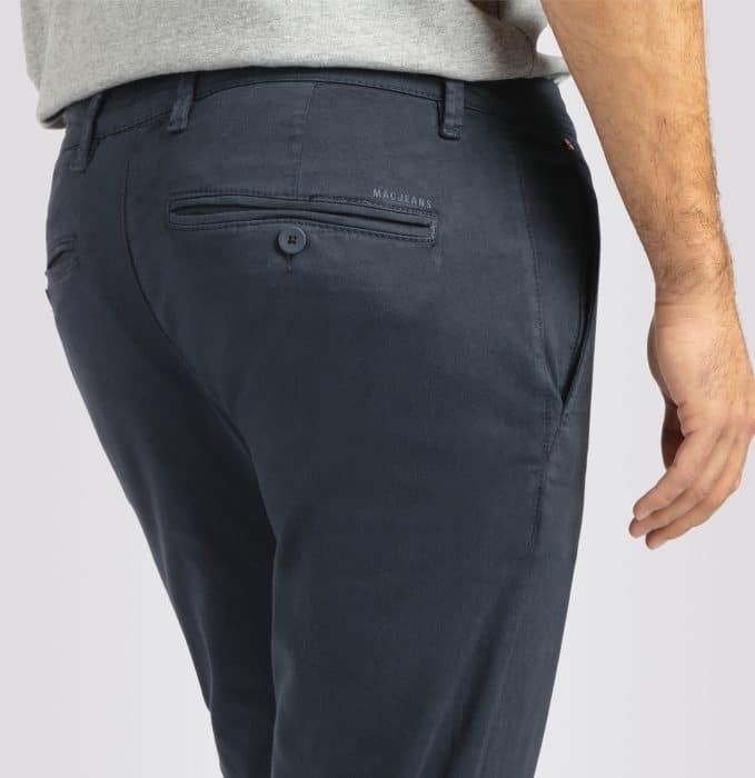 A person wearing navy blue dress trousers and a light grey shirt, shown from the waist down and viewed from behind. The trousers have back pockets, one with a button.