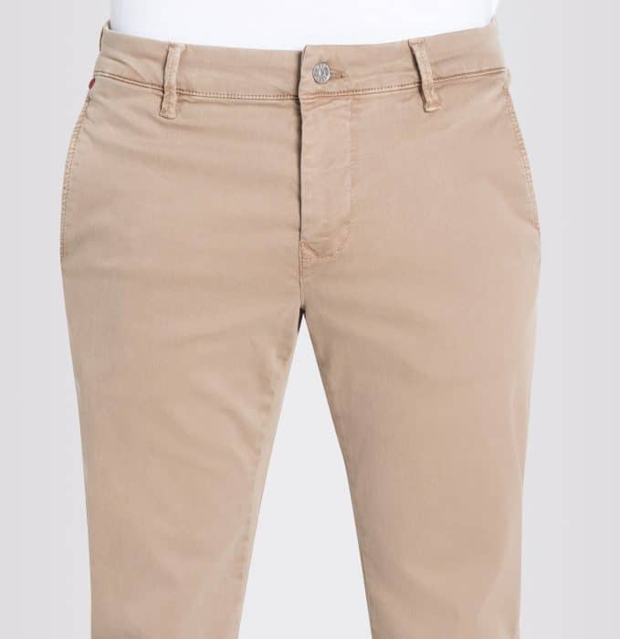 A close-up view of a person wearing light beige chinos, showing the waist and upper legs. The trousers have belt loops, side pockets, and a front button fastening. The background is plain and light-coloured.