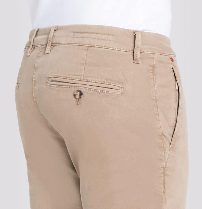A close-up view of the back and side of a person wearing light beige trousers with belt loops, a back pocket with a button, and a zippered side pocket. The person is also wearing a white shirt tucked in.