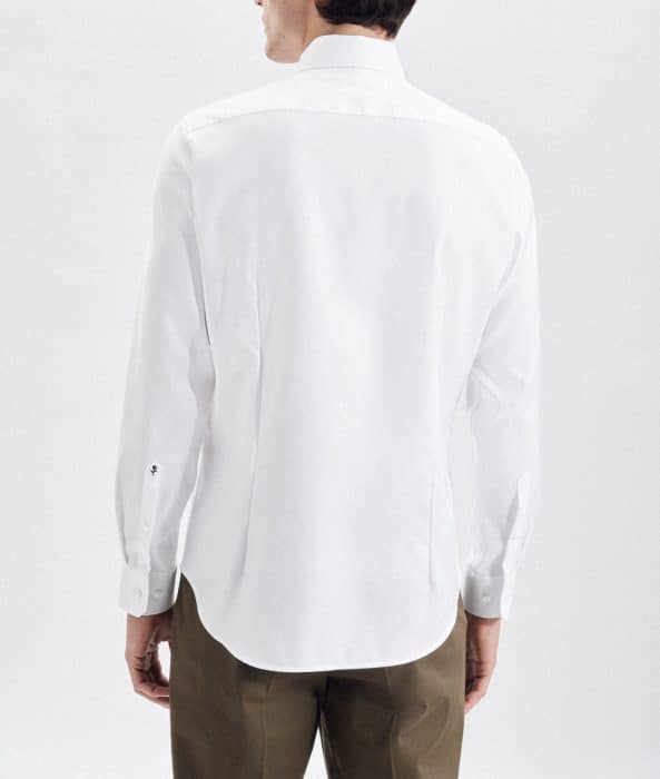 A person wearing a white long-sleeved button-down shirt and olive green trousers, shown from the back against a plain light background.