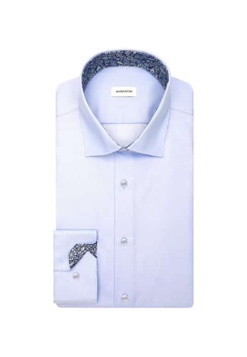 A light blue dress shirt neatly folded, featuring a contrasting dark blue floral pattern inside the collar and cuffs. The shirt has white buttons and a visible brand label inside the collar.