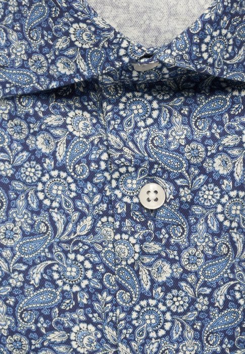 Close-up of a blue shirt with a white paisley and floral pattern, featuring a white button in the centre and part of the collar visible at the top.