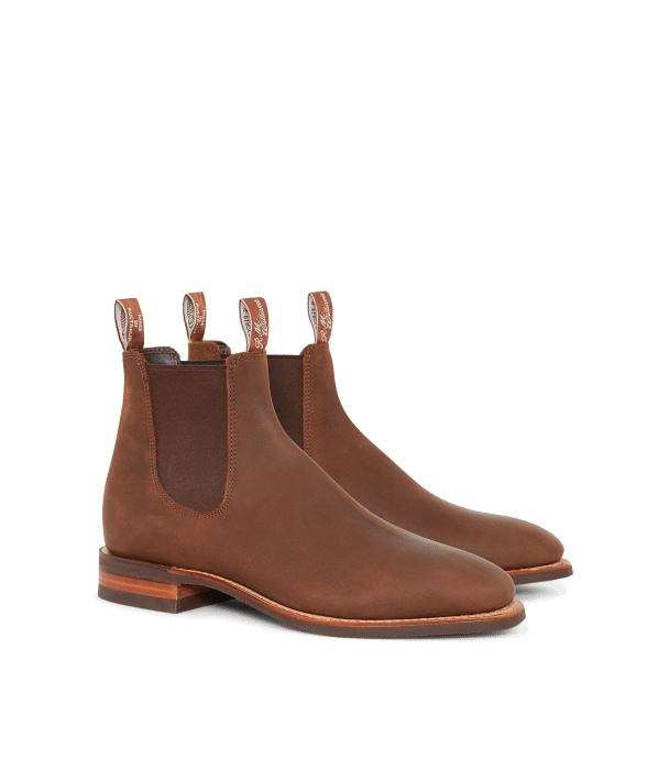 A pair of brown leather Chelsea boots with elastic side panels, pull tabs, and low stacked wooden heels, displayed on a white background.