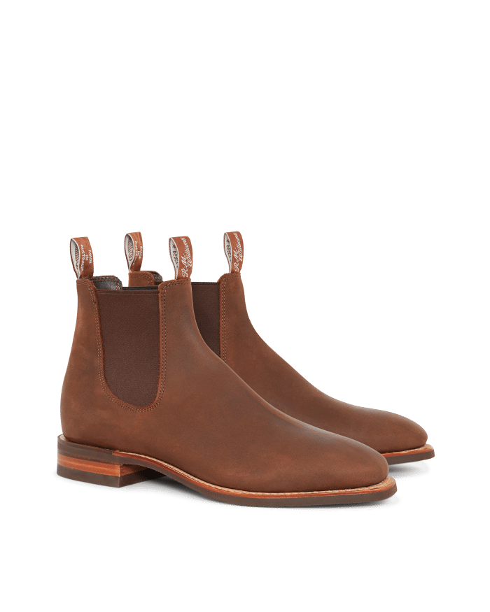 A pair of brown leather Chelsea boots with elastic side panels, pull tabs, and low stacked wooden heels, displayed on a white background.